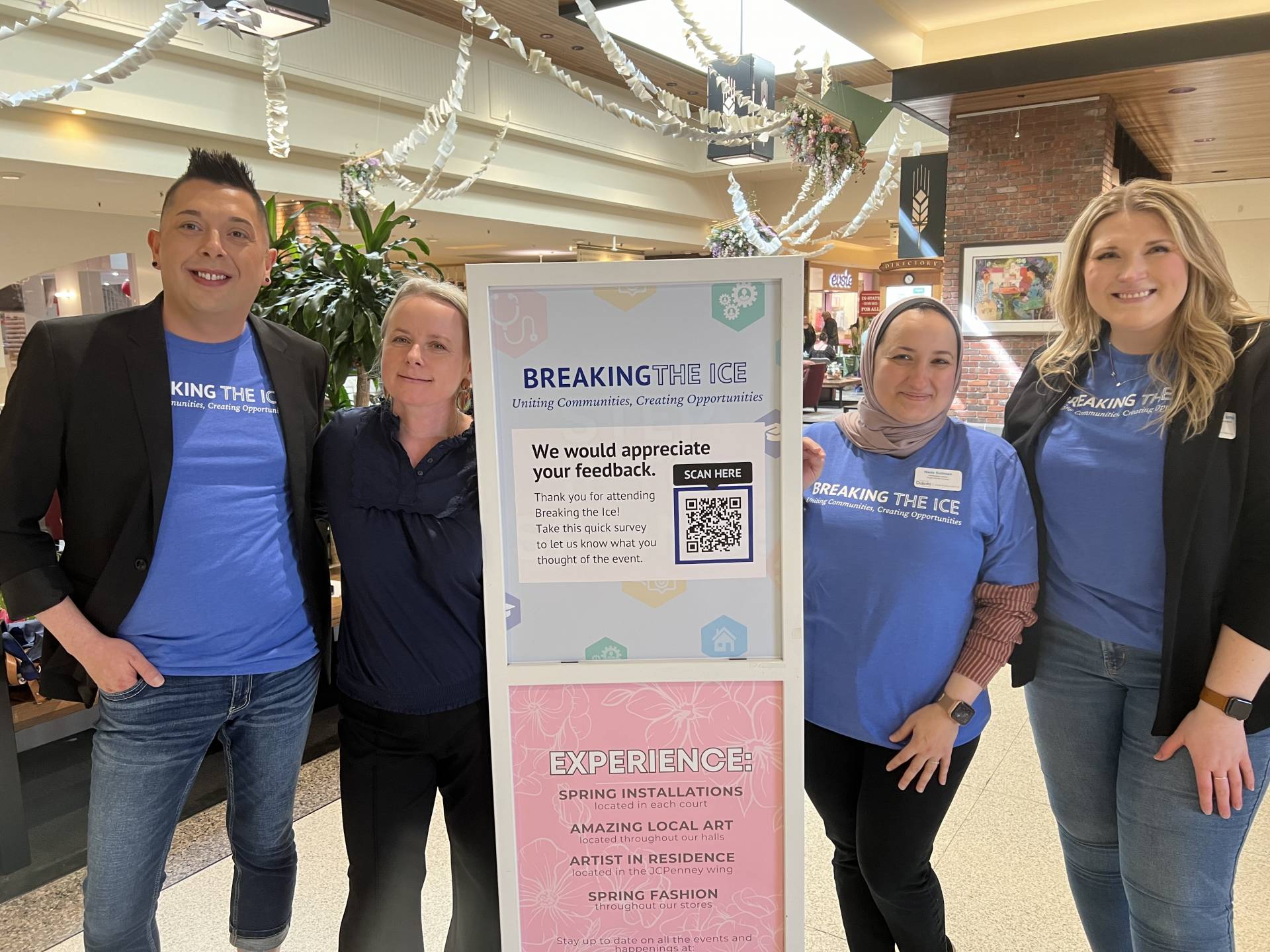 Three adult women and one adult man standing on either side of an event sign. All wearing a mix of blue and black.