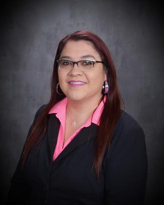 headshot of a Native American woman smiling with glasses, long hair, and a pink collared shirt under a black blazer