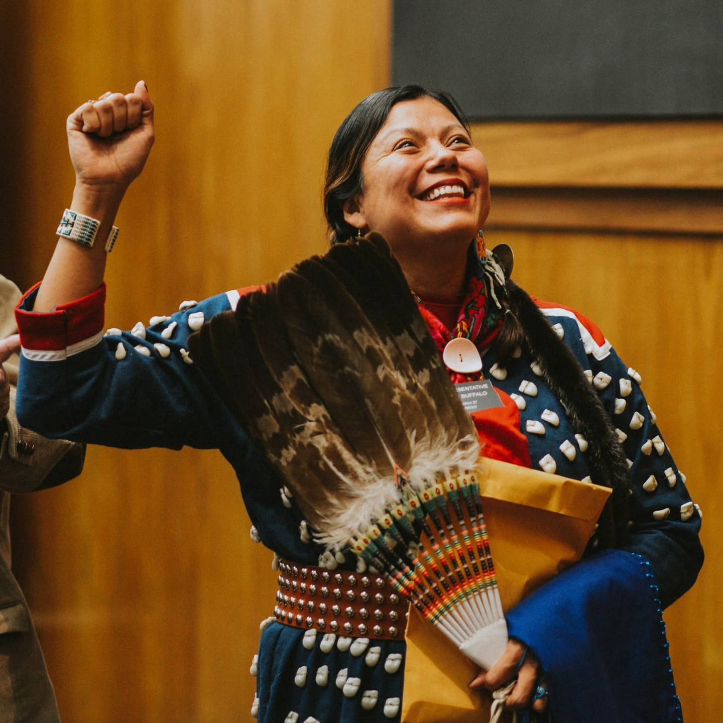 Native American woman in traditional dress smiling with her right hand up as she is sworn in