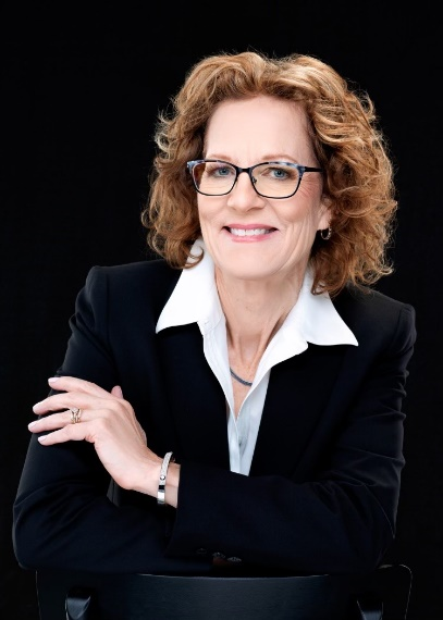 woman with curly hard and glasses smiling. She is wearing a black blazer and white button up.