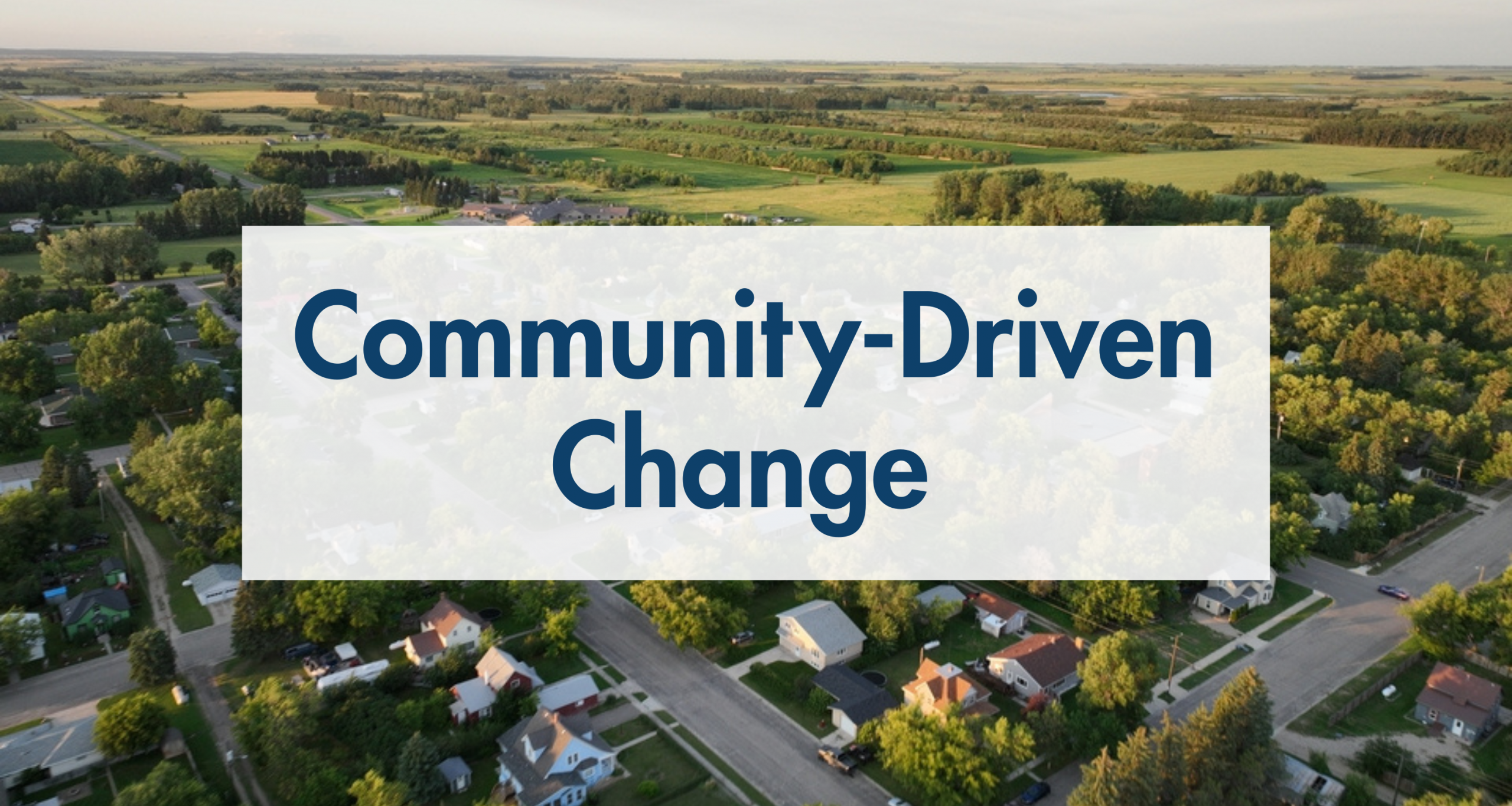 sky view of a rural ND town with the text "community driven change" overlayed in blue in a semi-transparent white box