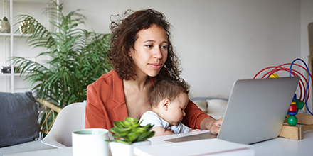 a mother using a computer while holding her daughter