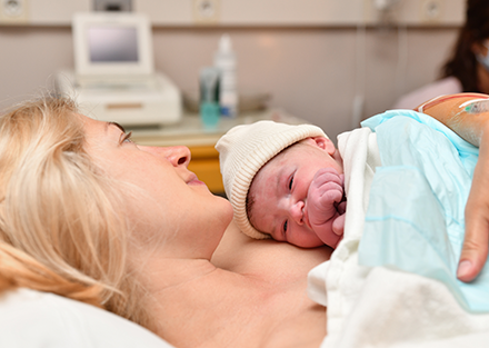 a new mother lays in a hospital bed, holding her infant to her chest