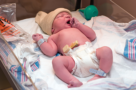 a newborn infant in a diaper and beanie sleeps in a hospital bassinet