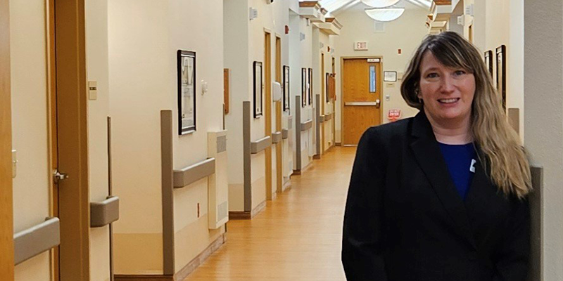 Woman in a black suit jacket standing in a long hallway at a nursing facility in New Salem, ND