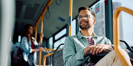 A dark-haired man with glasses happily riding public transit.