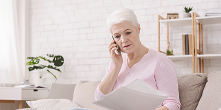 A woman with white hair and a pink shirt, making a phone call and reviewing paperwork.