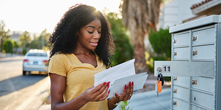 A dark-haired woman in a yellow t-shirt, checking her mailbox.