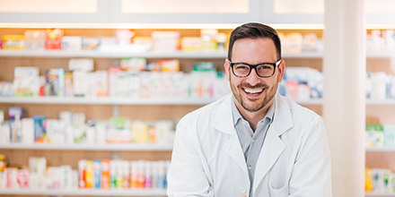 A pharmacist smiling in front of shelves of medications. 