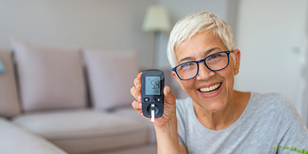  A woman smiling and holding a glucose monitor.