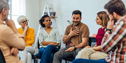 A group of people sitting in a circle, listening to a man share.