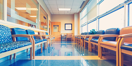 A waiting room with chairs lined against the walls and large windows.