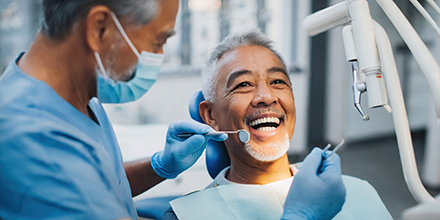 Man in a dental chair, smiling while his dentist prepares to clean his teeth.