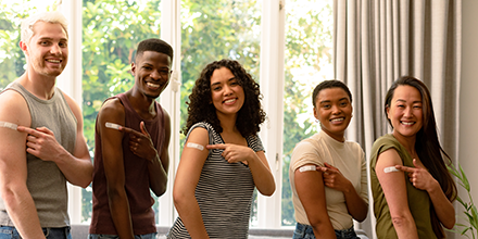 People lined up, smiling and pointing at their vaccine bandages