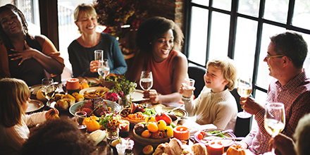 People of different backgrounds, sitting around a full Thanksgiving table, socializing.