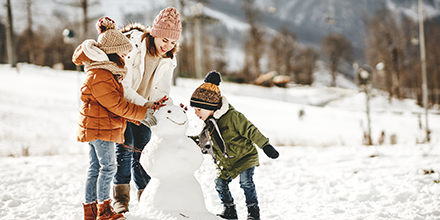 A woman and her children building a snowman.