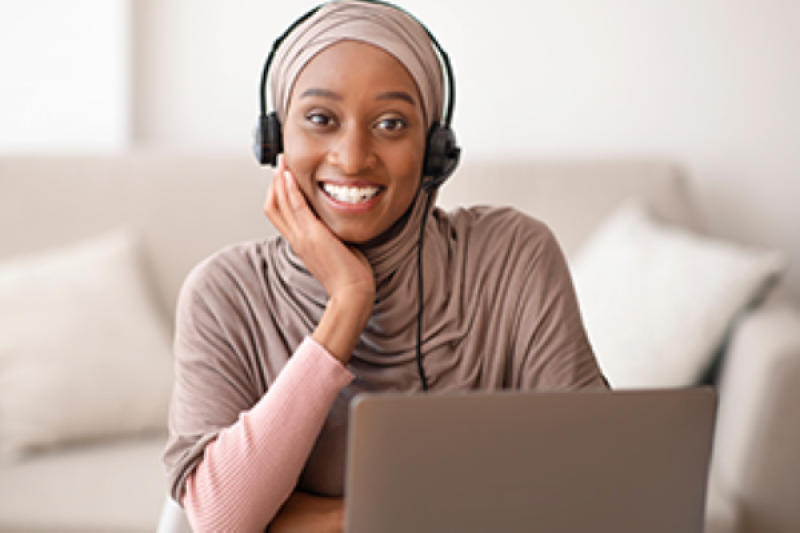 Young, smiling black woman wearing a head scarf working on a laptop computer