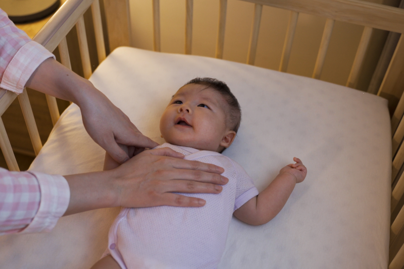 Hands reaching in to check on baby in a crib