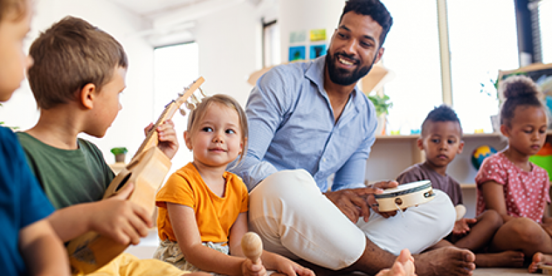 Male early childhood teacher sitting on floor with children